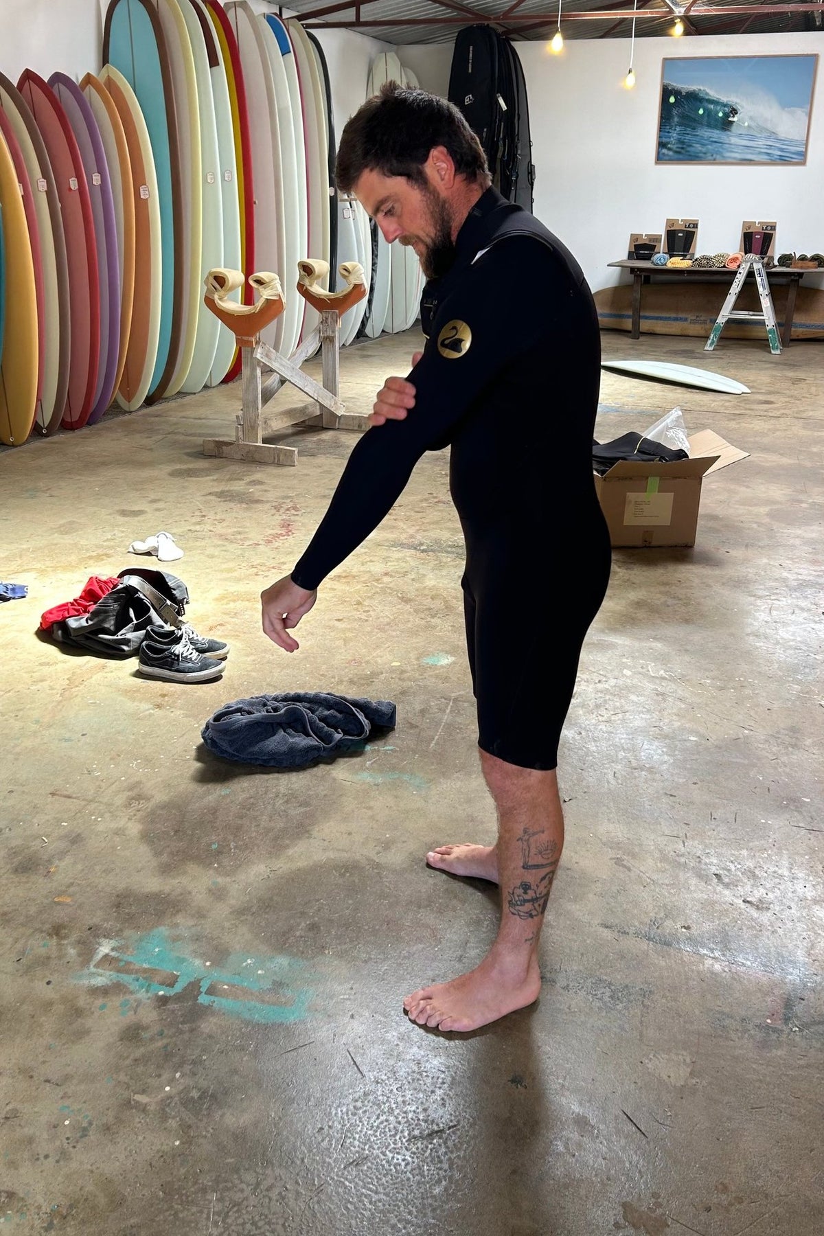 Surfer pulling on the Black Duck Long Sleeve 2mm Chest Zip Springsuit in the Moonshine Surfboards shop